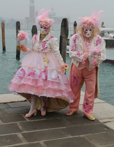 photo - carnaval de venise - zoom souvenirs - couple - robe - costume - masque - déguisement - plume - dentelle - gant - rose - violet - ponton - mer - poteau - bois - clocher -