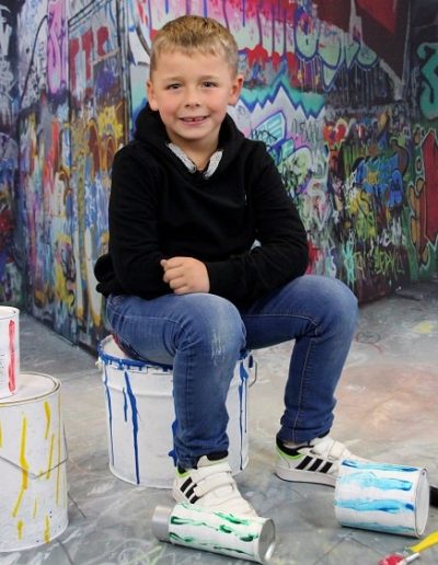 photo - scolaire - zoom souvenirs - enfant - peinture - pot - pinceau - garçon - sourire - pull - jean - rouge - noir - décor - graffiti - bleu