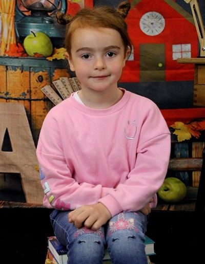 photo - scolaire - zoom souvenirs - enfant - sourire - fille - pull - jean- livre - décor - assis - rose - rouge - bleu