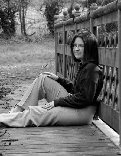 photo - extérieur - zoom souvenirs - fille - lunette - pont - sourire - assis - pull - pantalon - forêt - feuille - pelouse - noir et blanc
