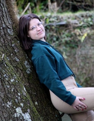 photo - extérieur - zoom souvenirs - arbre - fille - sourire - pull - pantalon - forêt - soleil - lunette - marron - vert