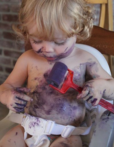 photo - thématique - zoom souvenirs - bébé - jeu - peinture - rouleau - salir - violet - blonde - violet - chaise - marron - boucle